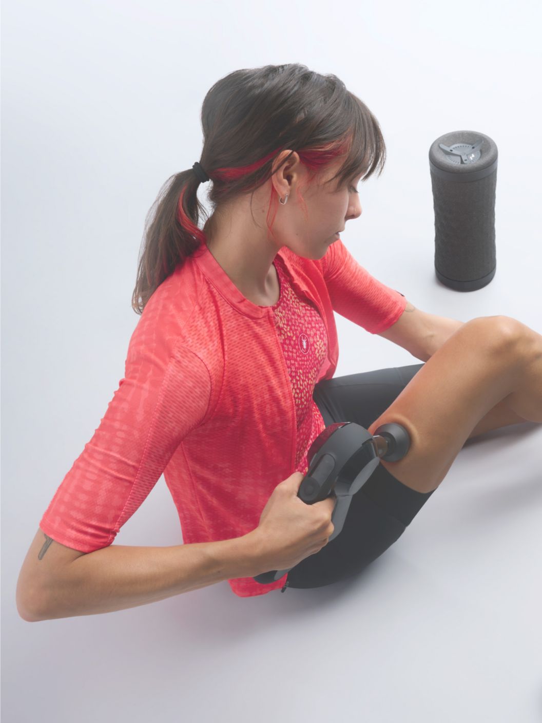 A rider sits on the floor while using a Theragun Elite percussion massager on their leg. A Hyperice massage roller is seen next to them. 